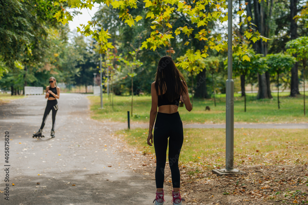 Obraz premium Two women in sportswear rollerblading at the park in sunny weather..