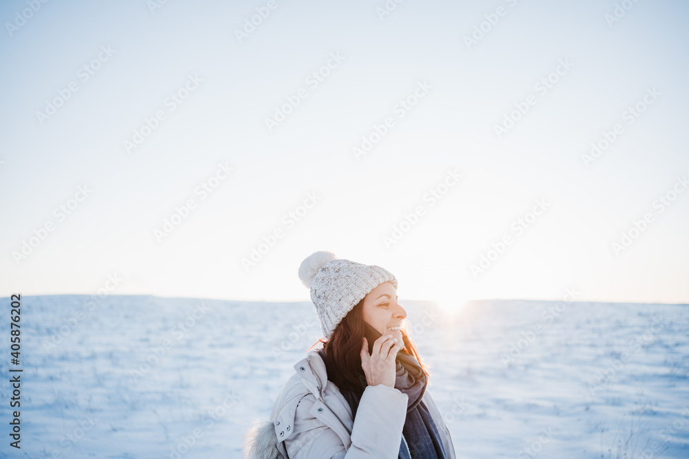 beautiful young woman at sunset in snowy mountain talking on mobile phone. Nature and technology concept. winter season