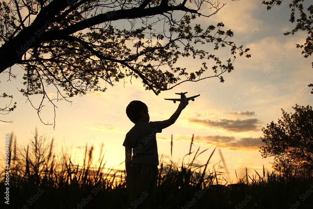 A little boy in silhouette holding airplane in field at gorgeous sunset symbolizing peace in the world