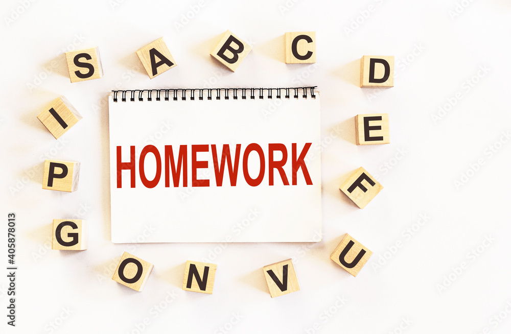 Text HOMEWORK, on notepad and white background, around are wooden cubes with letters Text HOMEWORK, on notepad and white background, around are wooden cubes with letters