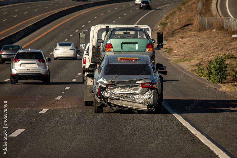 A car with extensive rear end damage being towed on a freeway A car with extensive rear end damage being towed on a freeway