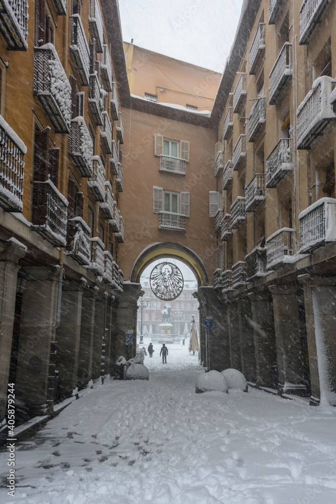 View of the access doors of the historic Plaza Mayor of Madrid covered with snow under a heavy snowfall.
