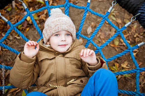 A cute preschooler boy in a knitted hat is playing in the Playground on an autumn day.