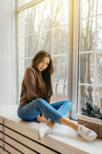 Young woman in hoodie posing in studio sitting on the windowsill © andrew_shots