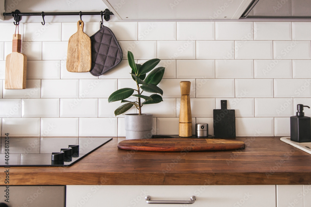 Kitchen brass utensils, chef accessories. Hanging kitchen with white tiles wall and wood tabletop.Green plant on kitchen background - obrazy, fototapety, plakaty 