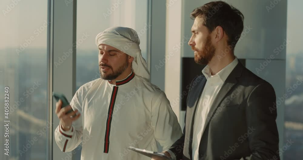 Multi-cultural couple of business colleagues meeting in modern office. Arabian entrepreneur investor talking on mobile phone. Multi-cultural couple of business colleagues meeting in modern office. Arabian entrepreneur investor talking on mobile phone.