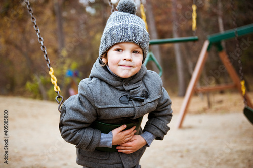 A cute preschooler boy in a knitted hat is playing in the Playground on an autumn day.