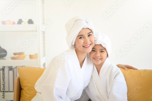 Happy beautiful mom and daughter in white bathrobe applying moisturizing cream on face at home, skin care and treatment concept