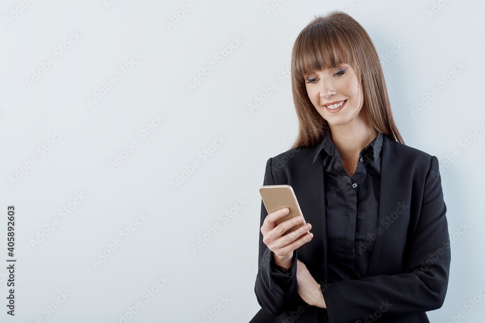 Business portrait of woman with phone - happy young white businesswoman in business casual standing against gray wall. Copy space for text. Business portrait of woman with phone - happy young white businesswoman in business casual standing against gray wall. Copy space for text.