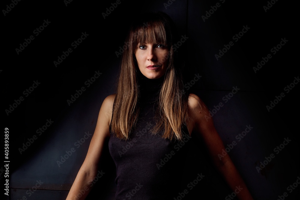 Beauty portrait of attractive young woman looking at camera, serious facial expression. Dark background.