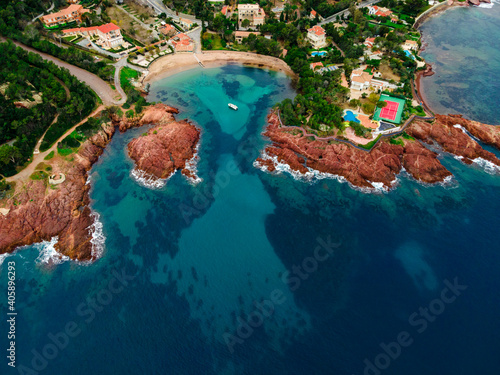 Aerial view of a small beach with turquoise waters, anchored small boat and red rocks, typical of the Esterel close to Cannes. picture taken in Agay, French Riviera, Côte d'Azur south of France