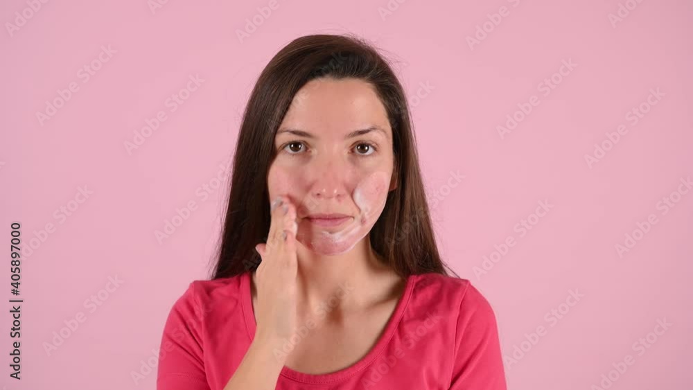 Woman smears her face with acne cream, on a pink background Woman smears her face with acne cream, on a pink background