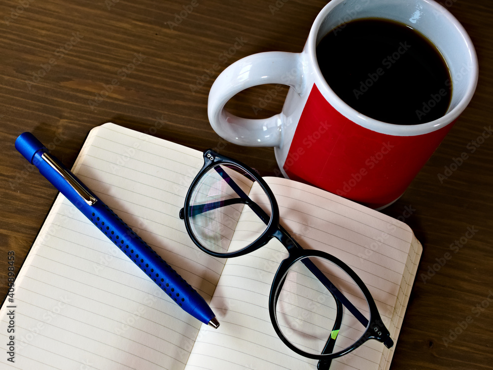 Offenes Notizbuch, Kugelschreiber, Brille zum Lesen und Schreiben, eine Tasse Kaffee auf einem Tisch Offenes Notizbuch, Kugelschreiber, Brille zum Lesen und Schreiben, eine Tasse Kaffee auf einem Tisch