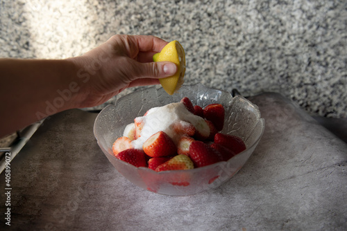 mano che spreme succo di limone su ciotola di fragole per preparare un dessert  photo