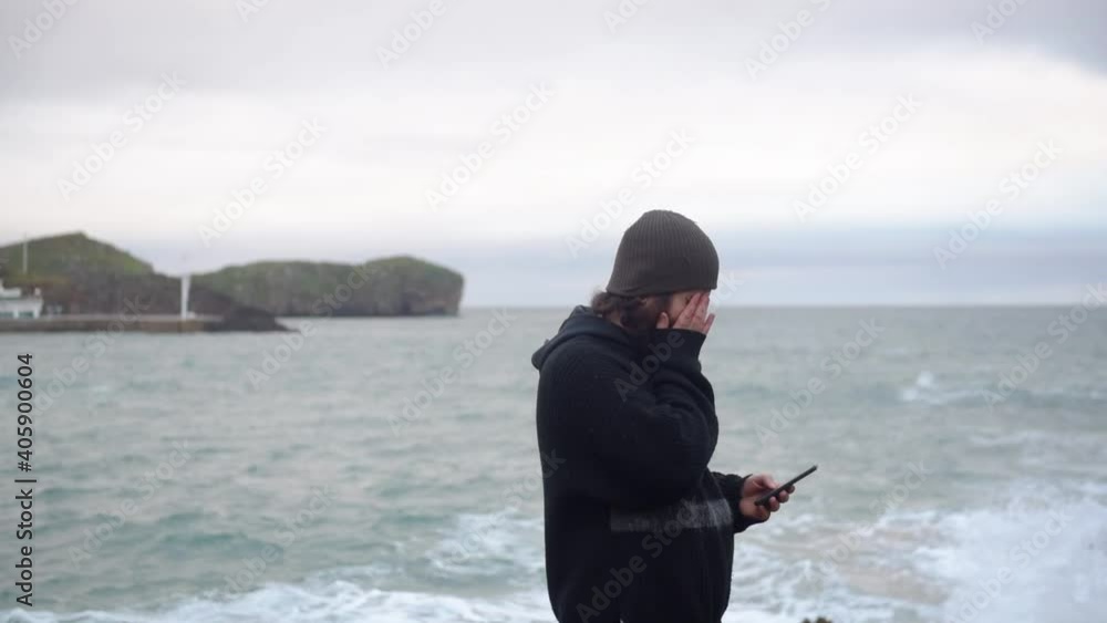 bearded man walking from left to right chatting on the mobile with his girlfriend and smiling with the sea in the background. communications and relationships concept bearded man walking from left to right chatting on the mobile with his girlfriend and smiling with the sea in the background. communications and relationships concept
