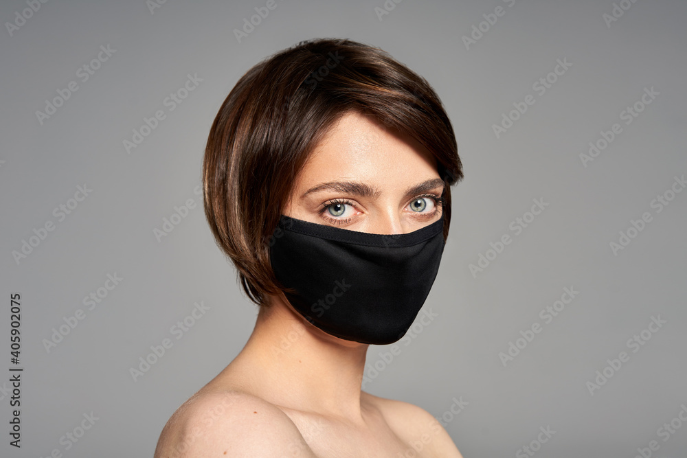 Close-up portrait of girl with black reusable virus protective mask isolated over gray background Close-up portrait of girl with black reusable virus protective mask isolated over gray background