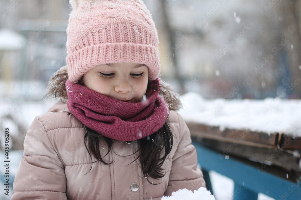 Warmly dressed little girl with a pile of snow in her hands outdoors during a snowfall