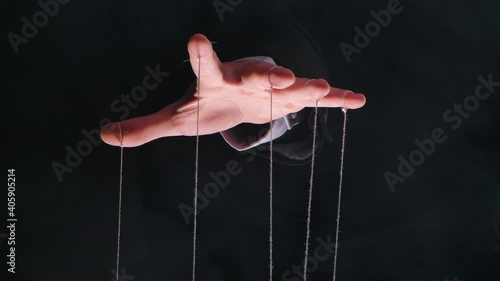 Hand of dictator in a business suit with strings on the fingers to control the puppet. Close up male hand with strings of marionettes on smoke black isolated background. Slow motion.