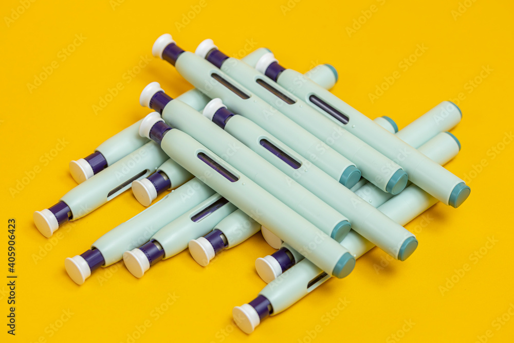 Grouping of a bunch of syringe self application injector pens on seamless yellow background. Studio medical equipment still life concept.