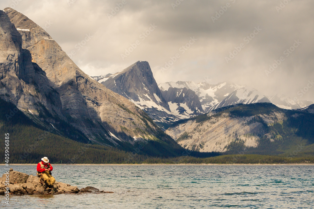 Lone Fly-fisherman changes fly on the shores of Upper Kananaskis Lake in the Rocky Mountain region of Alberta