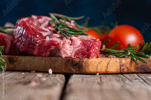 Close-up of raw pork or beef meat with tomatoes and rosemary on wooden cutting board o blue background. Image for butcher shop. Appetizing view for advertising.