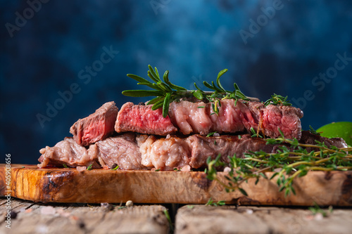 Medium rare grilled beef steak ribeye with rosemary on wooden cutting board on dark blue background. Appetizing image for restaurant menu. Delicious food. Juicy meat.