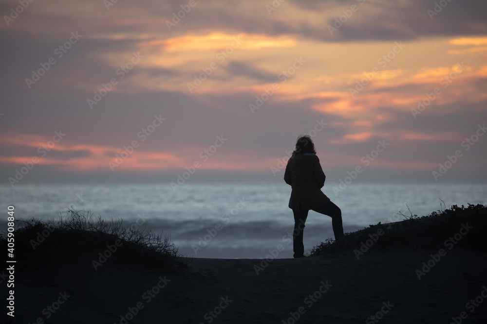 silhouette of a woman alone on a hill at the beach looking at ocean during sunset