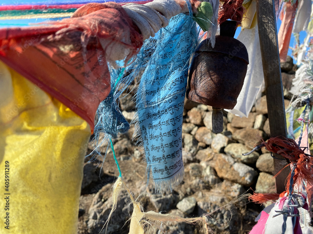 Close up of tattered Tibetan prayer flags with rusty metal bell hanging on line with rocks in backgroun