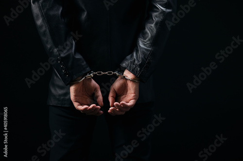 Close up of male prisoner with handcuffs over black background. Arrested man because of illegal action. Focus on hands. © MYDAYcontent