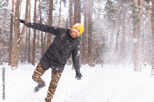 An adult brutal man with a beard in a forest covered with snow, enjoying a beautiful day and magnificent winter weather