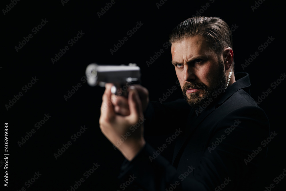 Serious bearded man aiming with gun over black background. Criminalist in black suit holding weapon in studio. Crime concept. Serious bearded man aiming with gun over black background. Criminalist in black suit holding weapon in studio. Crime concept.