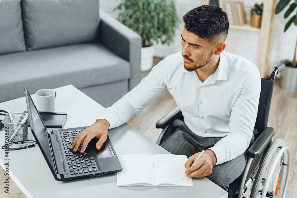 Positive disabled young man in wheelchair working in office Positive disabled young man in wheelchair working in office