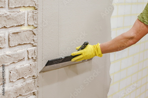 Plasterer smoothing  plaster  on wall for making texture of torn brick made of cement plaster by hand. Tape under plaster on wall to imitate decorative brick. home repair