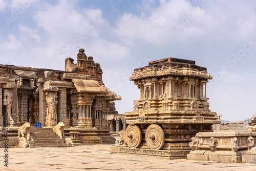 Hampi, Karnataka, India - November 5, 2013: Vijaya Vitthala Temple. Brown stone chariot in front of sanctuary under blue cloudscape.