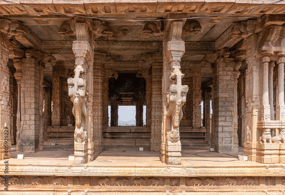 Hampi, Karnataka, India - November 5, 2013: Vijaya Vitthala Temple. Strait shot into brown stone abandoned and ruinous mandapam with sculpted pillar up front.