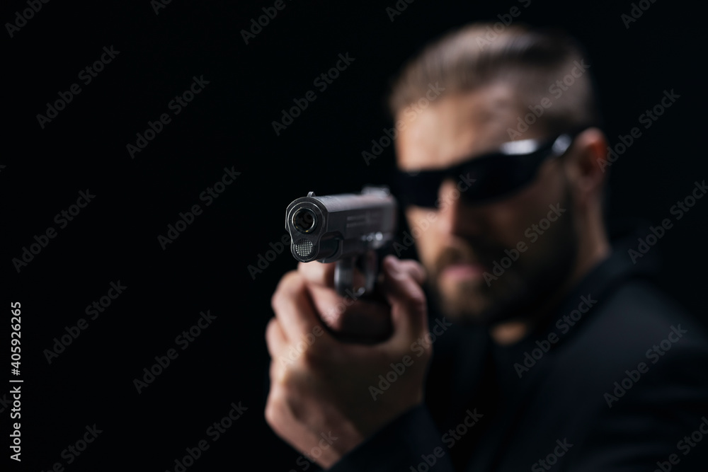 Brutal bearded man in sunglasses and suit aiming with gun over black studio background. Concept of mafia and criminal. Brutal bearded man in sunglasses and suit aiming with gun over black studio background. Concept of mafia and criminal.