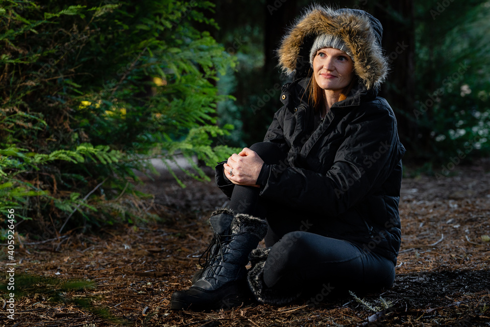Women Sitting on ground in Cold Forest with Warm Jacket possibly next to fire alone. Women Sitting on ground in Cold Forest with Warm Jacket possibly next to fire alone.