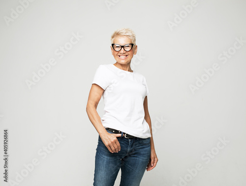 Fényképezés Aged people, lifestyle and maturity concept: blonde fifty year old European female with stylish pixie haircut and eyeglasses smiling at camera and posing isolated over grey background