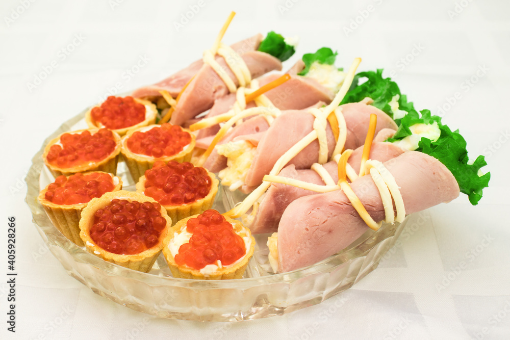 Snacks on a plate, selective focus. Red caviar in tartlets. Ham rolls with cheese.
