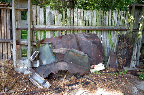 Remnants of an automobile leaning against an old slatted wooden fence in a back yard Rzeczyca Poland