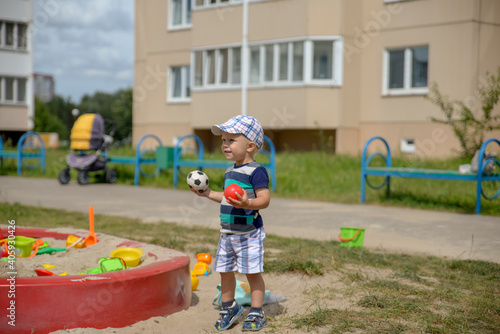 A boy in shorts and a cap plays in a sandbox with toys