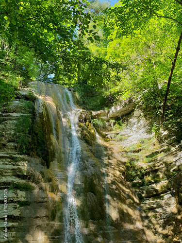 a stream of water falling from a mountain covered with green bushes and trees and forming a waterfall