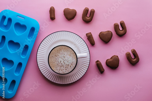 handmade chocolate candies, mold and coffee on pink backdrop, candymaking concept: i love you shape confectionery mold. idea for Valentine's Day, wedding, anniversary, Love symbol.