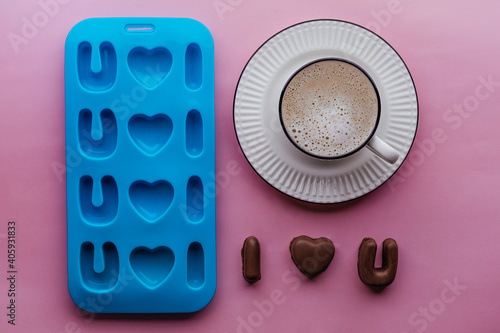 handmade chocolate candies, mold and coffee on pink backdrop, candymaking concept: i love you shape confectionery mold. idea for Valentine's Day, wedding, anniversary, Love symbol.