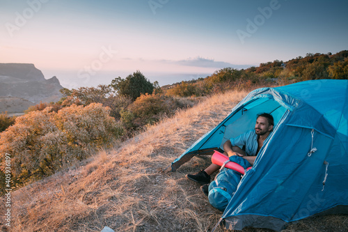 Young male tourist with a backpack in a tent in the mountains