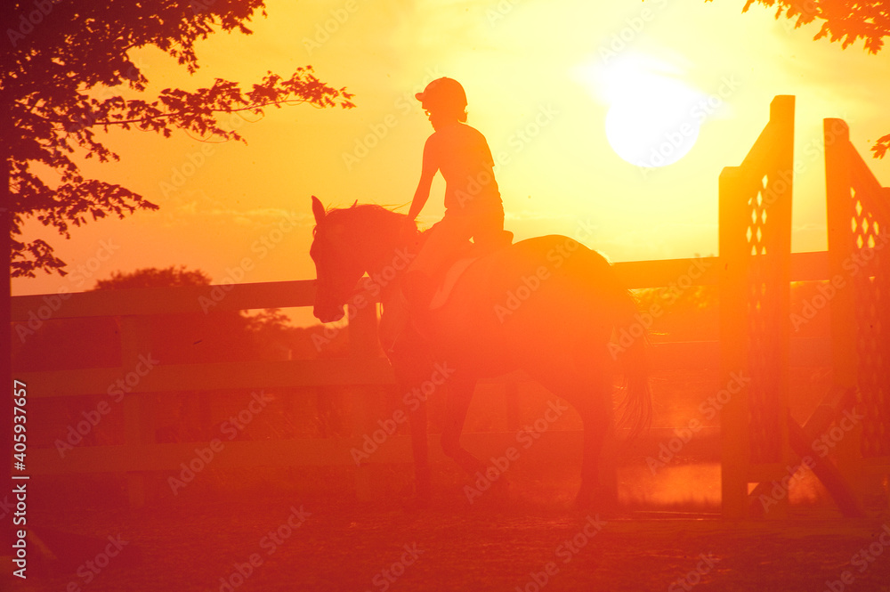 SIlhouette of young girl riding horse over low jumps