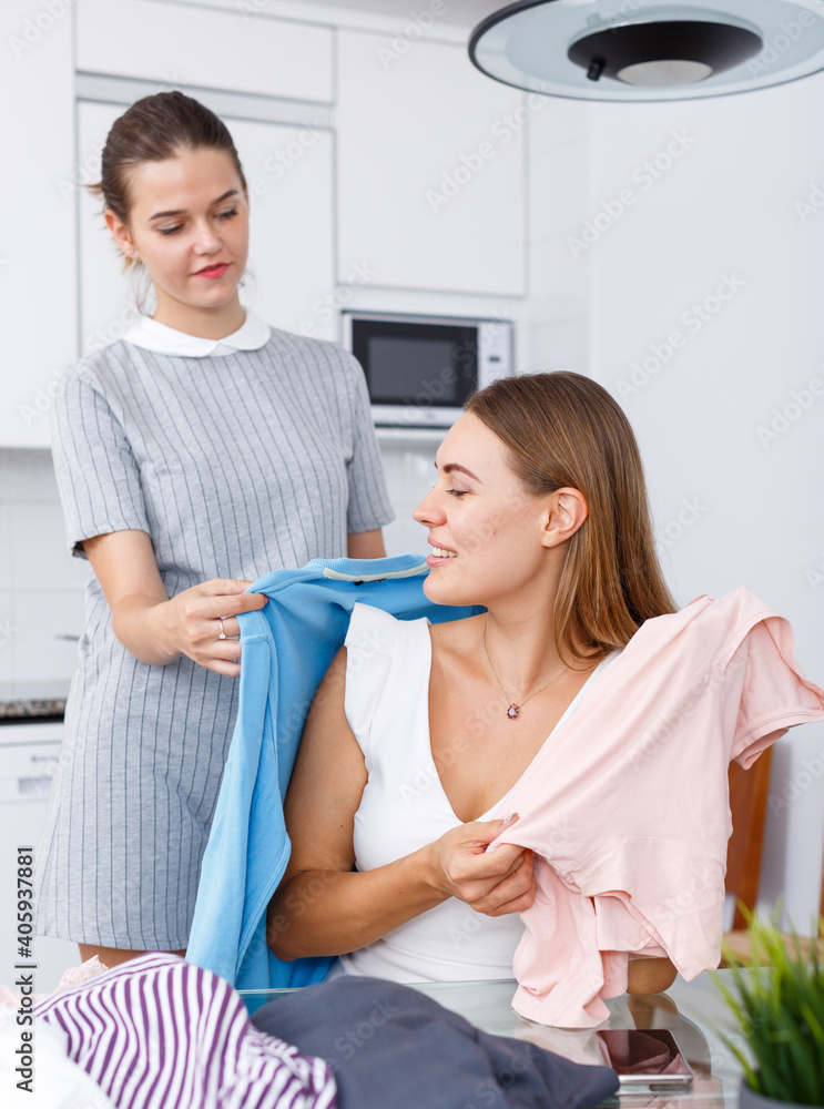 Two modern girls showing each other clothes in kitchen interior