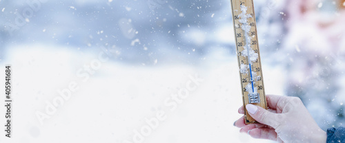 A young adult woman hold in her hand snowy thermometer showing a temperature slightly below freezing. The joy of snow.