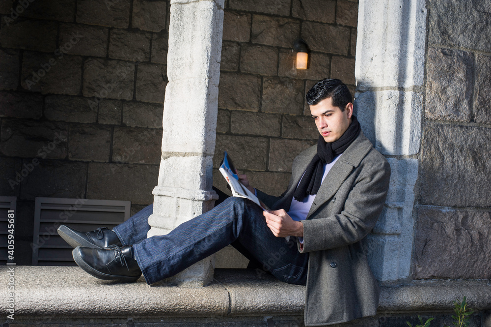 A young guy is sitting on a old window frame and reading.