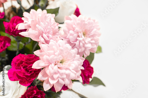 Closeup pink flora in a bunch of colorful mixed flowers and green leaves on white background, depth of field. Beautiful fresh floral decorating for a romantic anniversary celebration with copy space.